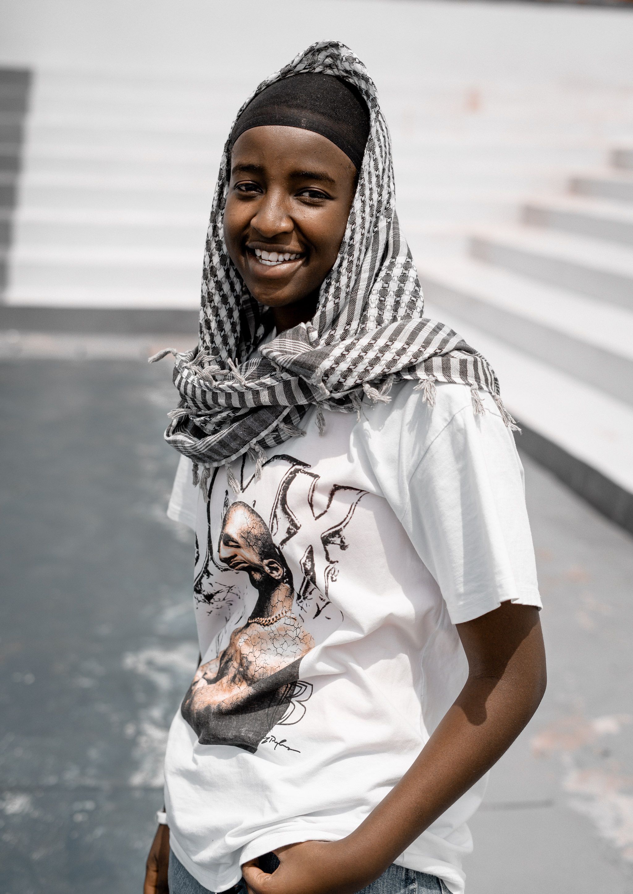 A cheerful young man wearing a striped headscarf and casual t-shirt standing outdoors on steps.