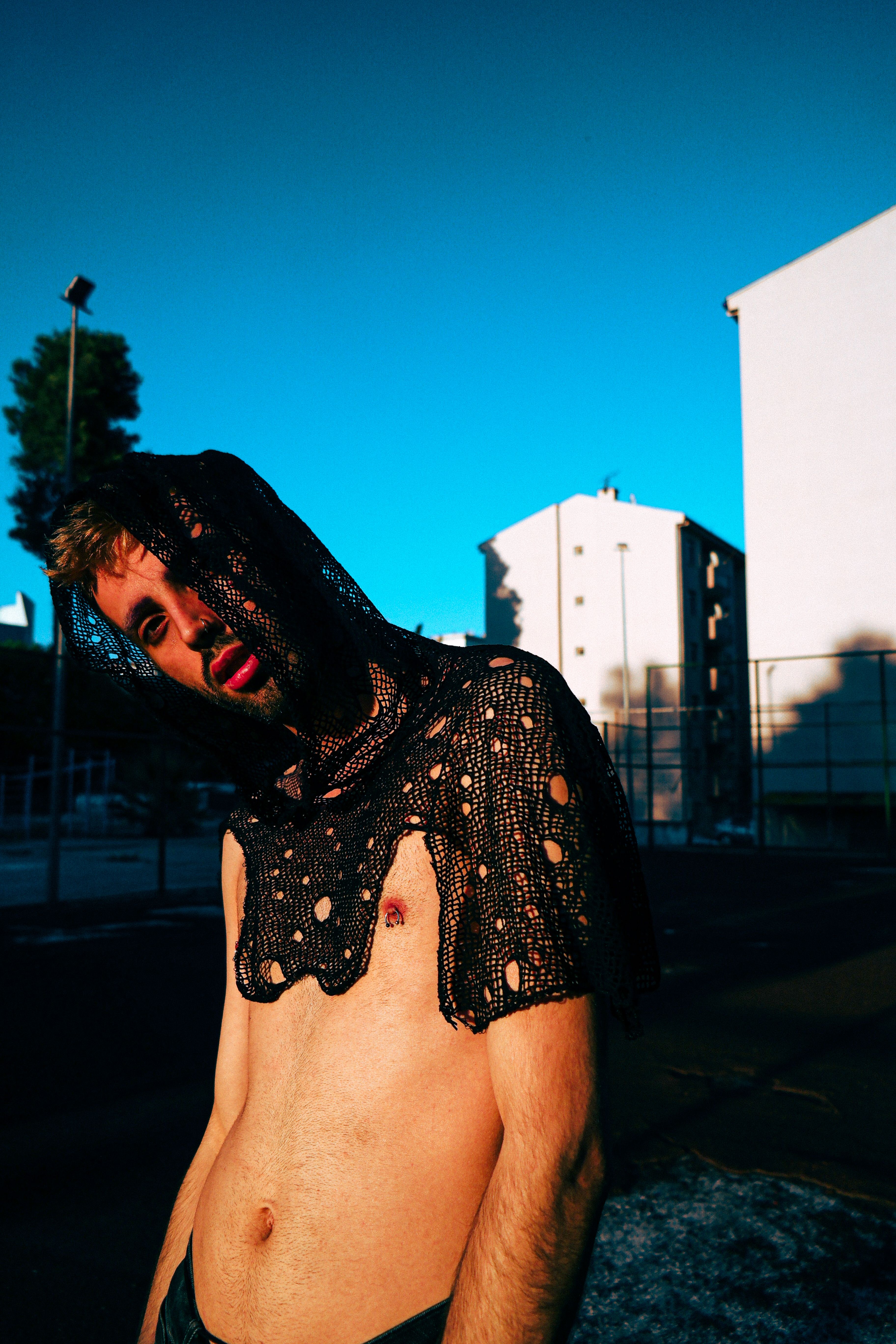 A shirtless man wears a netted hood in a vibrant urban portrait.