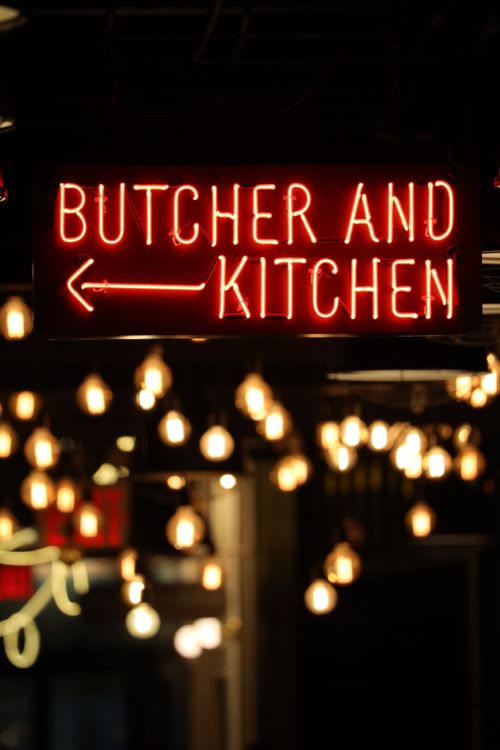 Free A glowing neon sign reading 'Butcher and Kitchen' against a blurred bokeh background of lights. Stock Photo