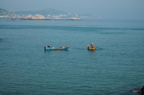 Free Fishing boats with nets cast on a tranquil blue sea with a distant coastal view. Stock Photo