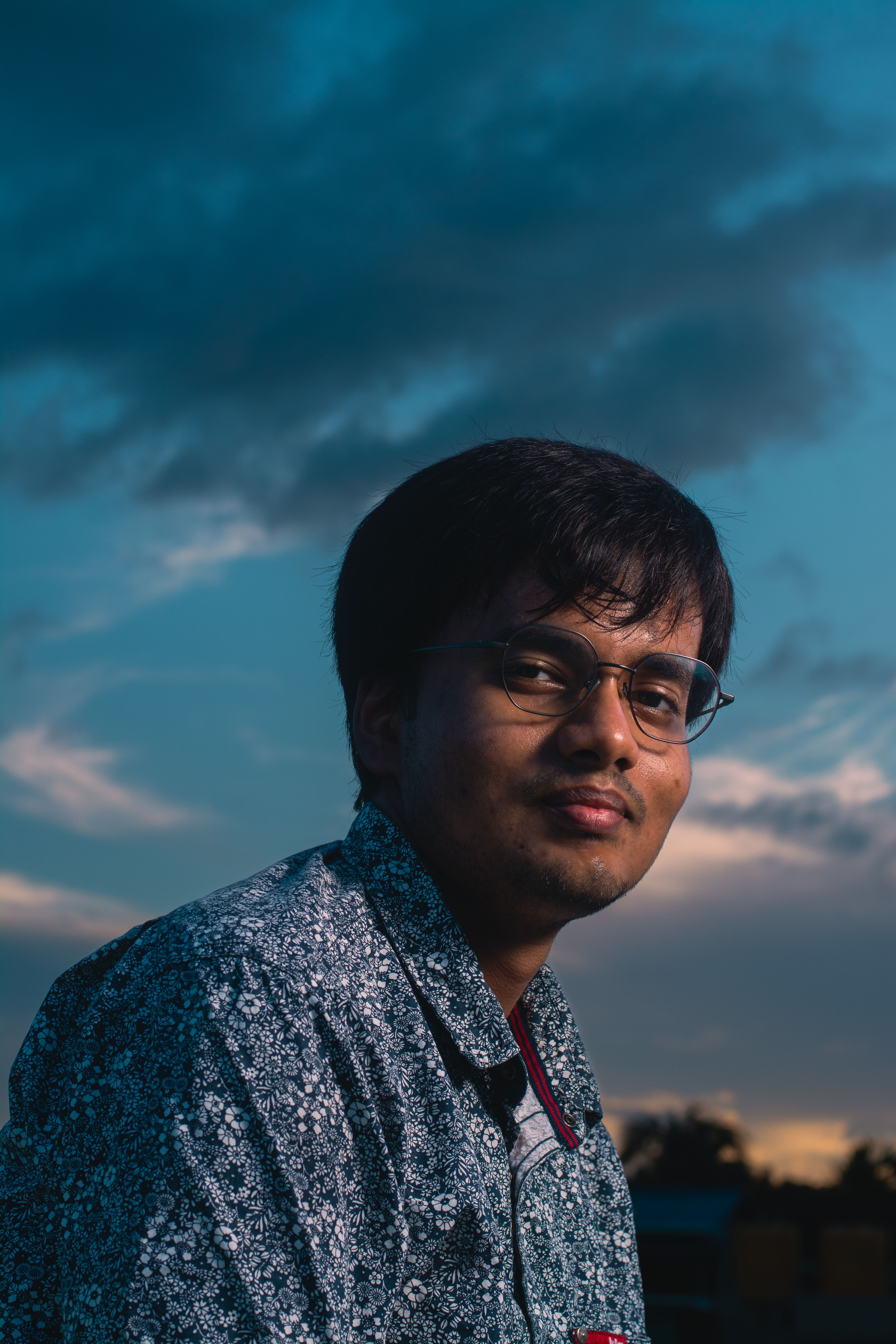 Portrait of a man with glasses against a dramatic twilight sky, exuding relaxation.