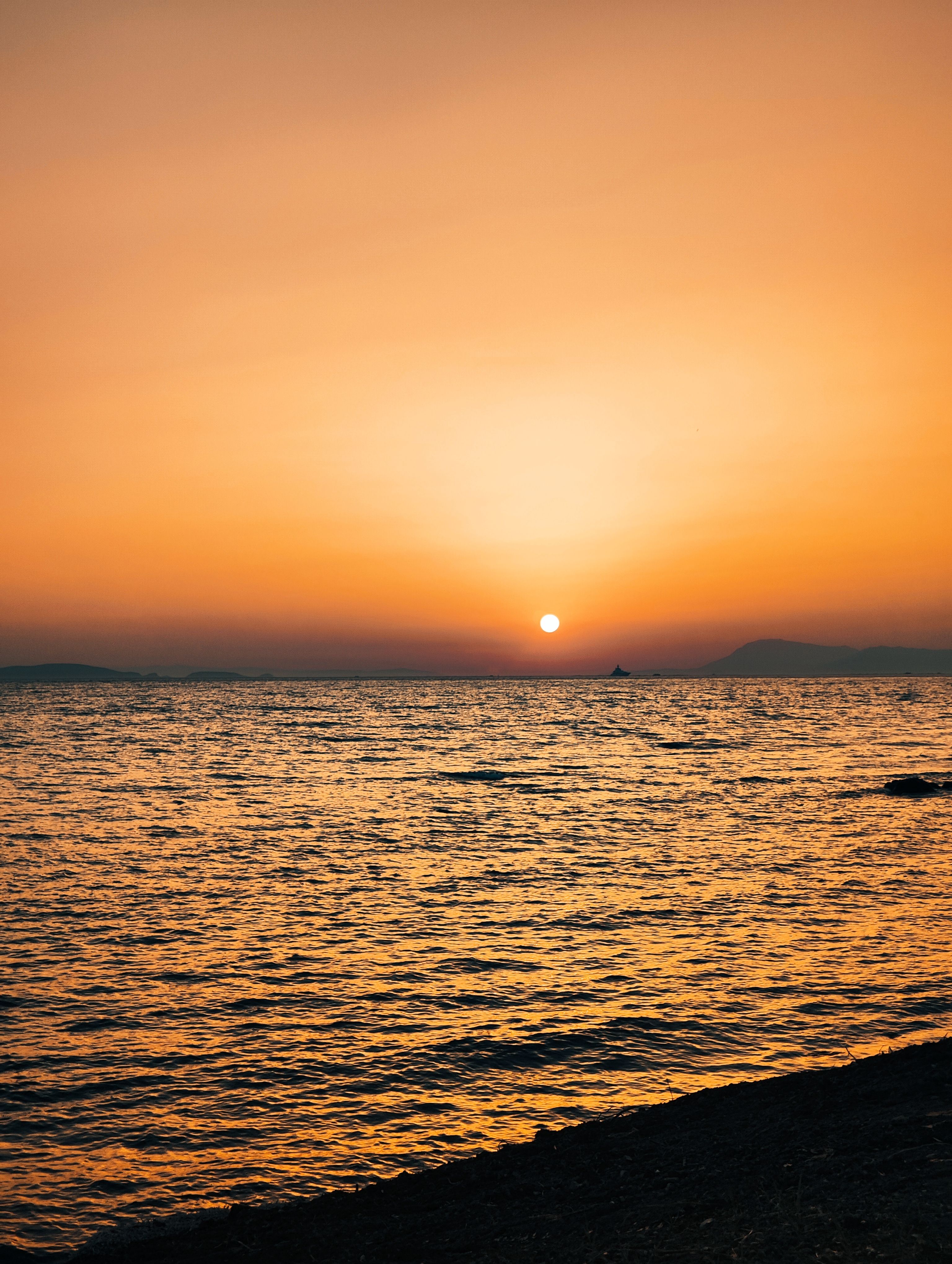 Beautiful sunset over the Aegean Sea in Didim, Türkiye with a vibrant orange sky.
