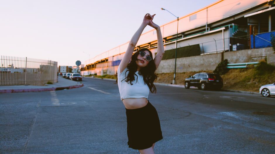 A fashionable young woman poses confidently on a Tijuana street during sunset.