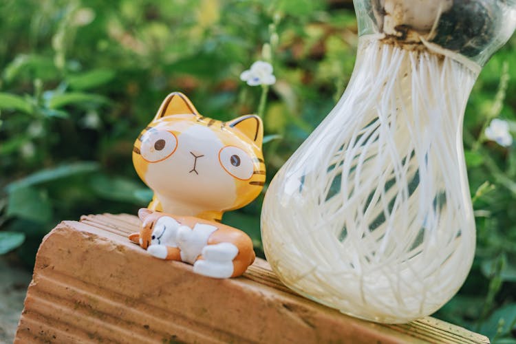 Yellow Cat Figurine Beside Clear Glass Vase