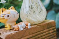 一只可爱的陶瓷猫雕像摆放在质朴的砖面上，背景是模糊的绿色