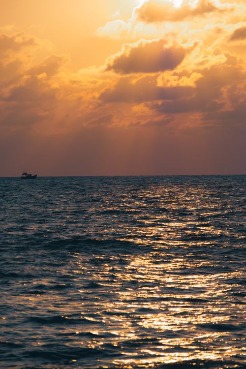 Free A calming sunset scene over a sea with golden reflections and a distant boat. Stock Photo