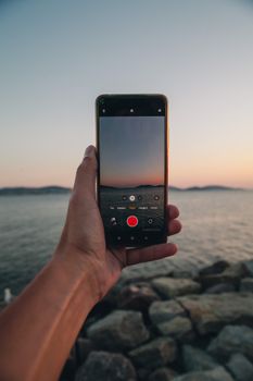 Person holding a smartphone recording a serene sunset by the sea in Istanbul.