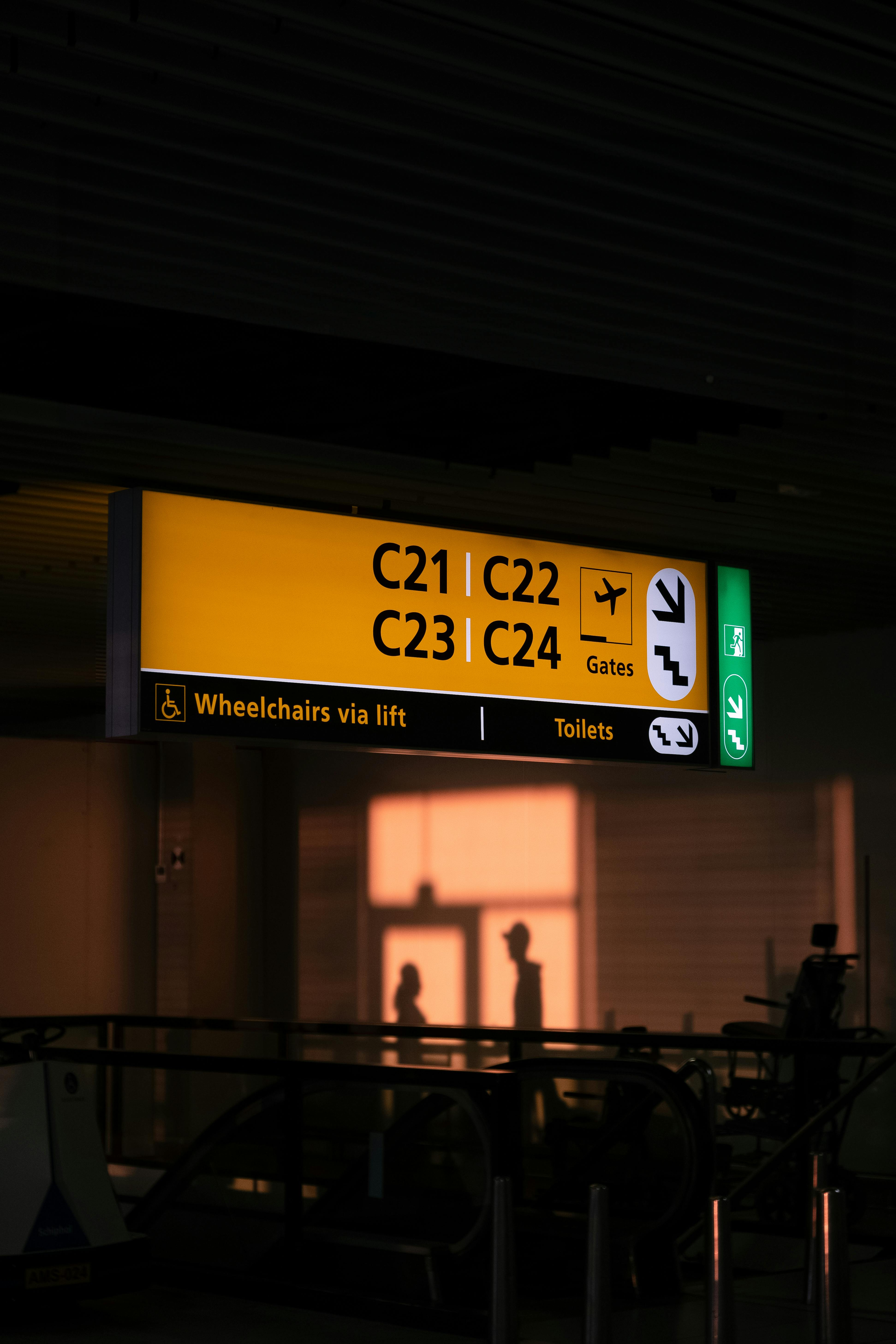 Silhouettes of travelers by a terminal sign in a dimly lit airport, illustrating travel ambiance.