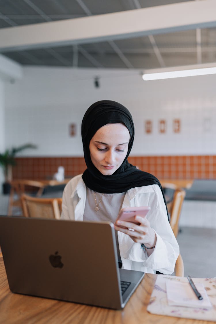 Young Woman In Hijab Sitting At A Table With Laptop And Smart Phone