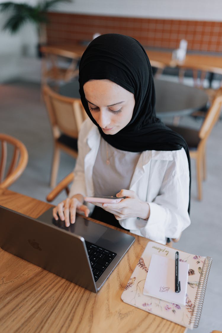 Young Woman In Black Hijab Working On A Laptop At A Cafe Table