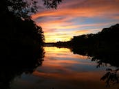 平静的湖泊倒映着美丽的日落与绚烂的色彩，四周环绕着树木的剪影