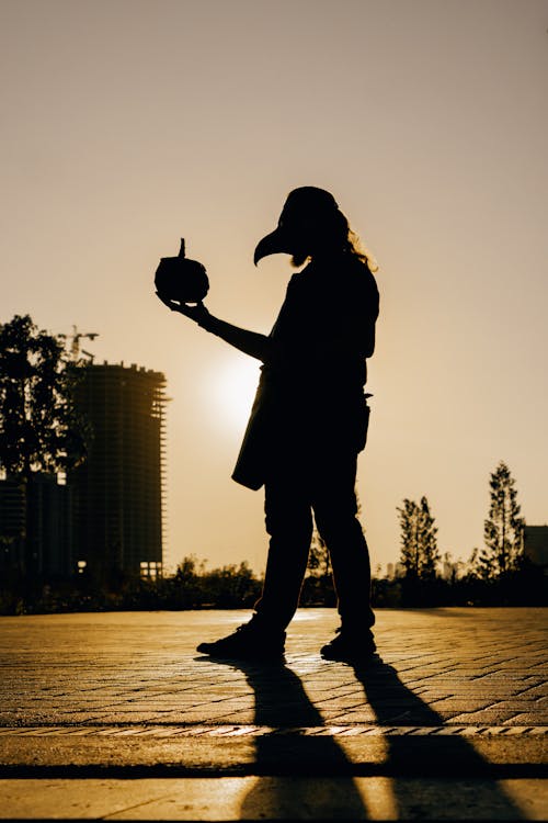 Silhouette of a Person in a Beaked Mask Holding a Pumpkin