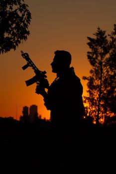 A silhouette of a man holding a paintball marker with a sunset background, evoking adventure and leisure.. silhouette, holdin