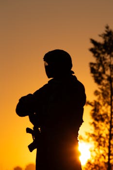 Backlit silhouette of a paintball player at sunrise, capturing an action-ready pose.