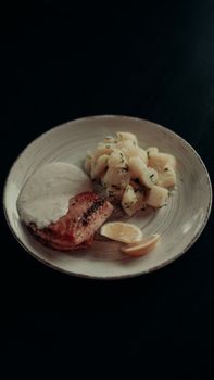 A beautifully arranged dish of salmon with creamy sauce and diced potatoes on a sleek plate.