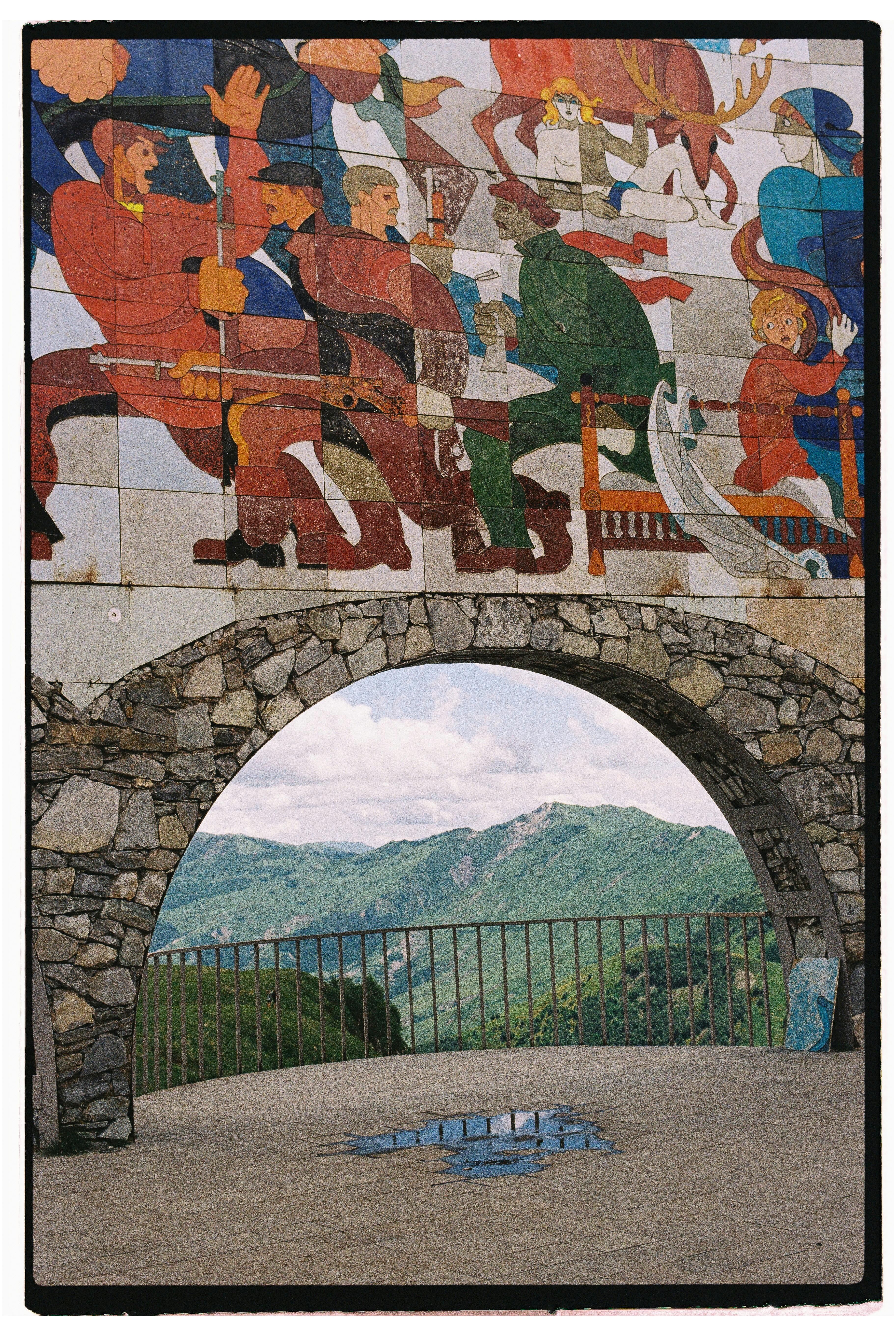 Colorful mosaic and stone arch offering a scenic mountain view, perfect for travel and art themes.