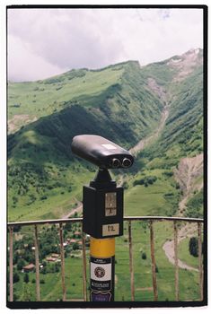 Binoculars on a terrace offer a view of lush green mountains in summer.