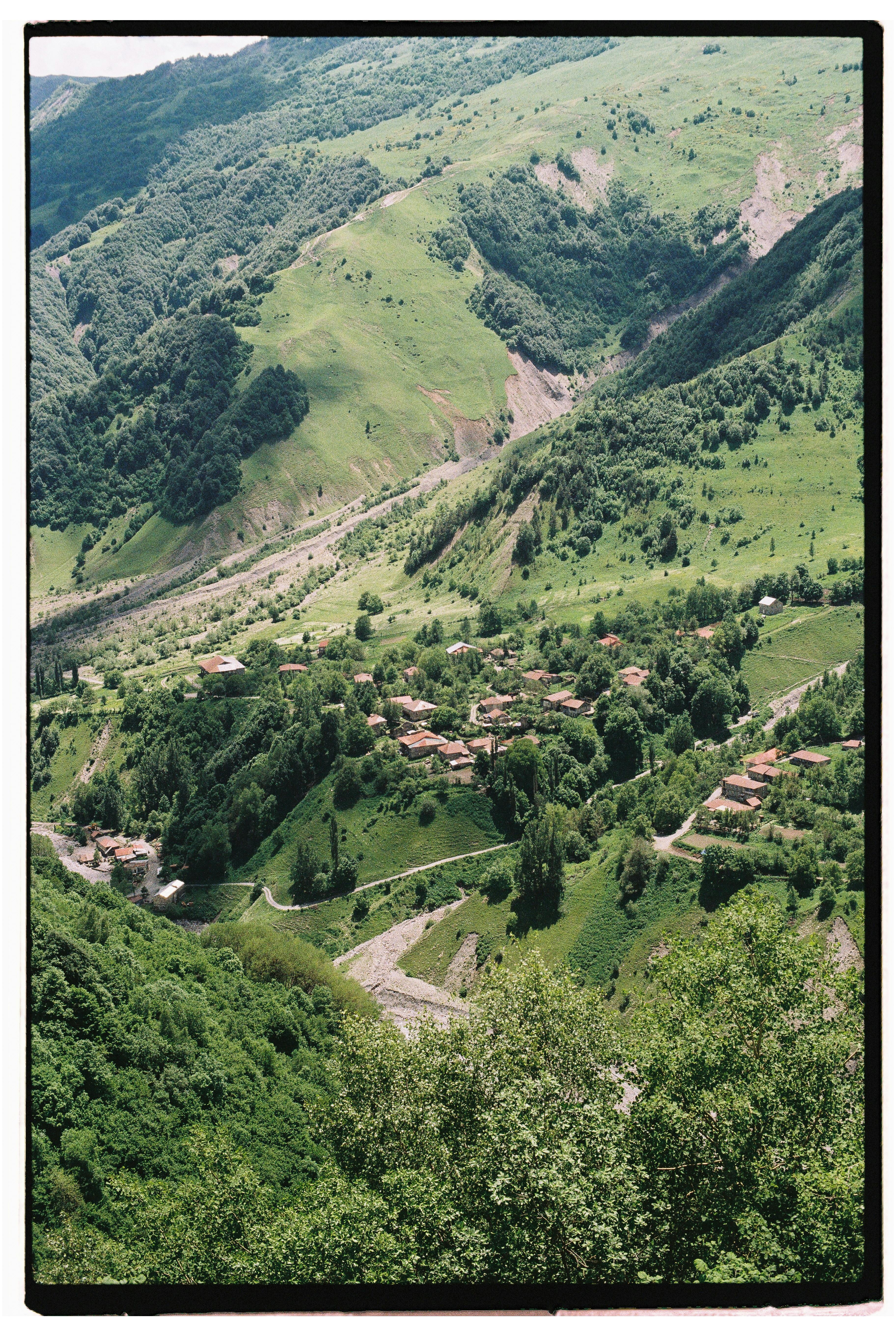 A breathtaking aerial view of a verdant valley with a small village nestled among green hills and mountains.