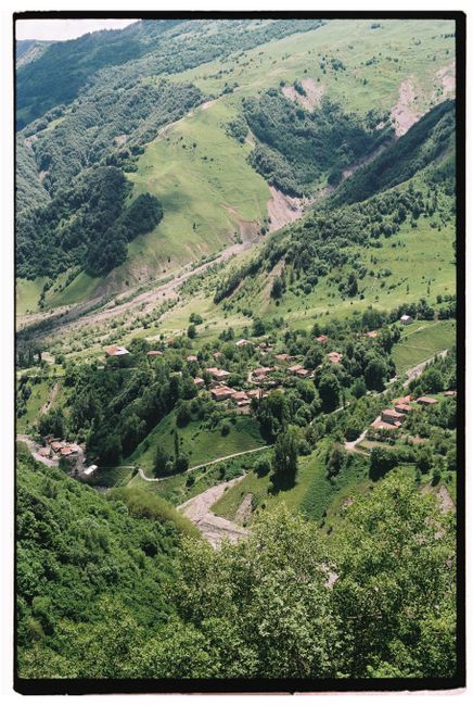 A breathtaking aerial view of a verdant valley with a small village nestled among green hills and mountains.