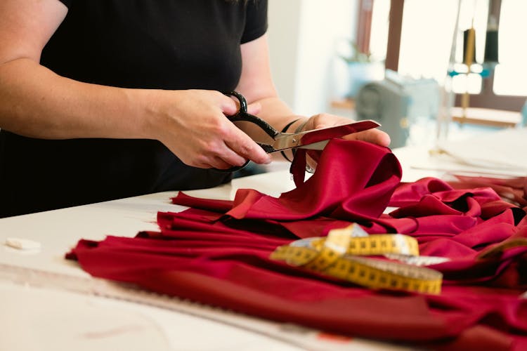 Tailor Cutting A Red Fabric With Scissors