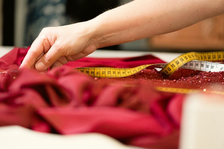 Woman Measuring A Red Fabric With A Tape