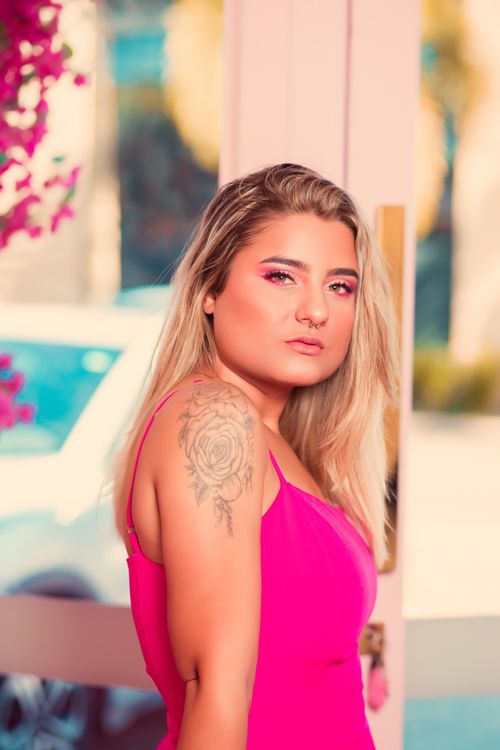 Free Fashionable woman with tattoo and blonde hair posing in a vibrant pink dress outdoors. Stock Photo