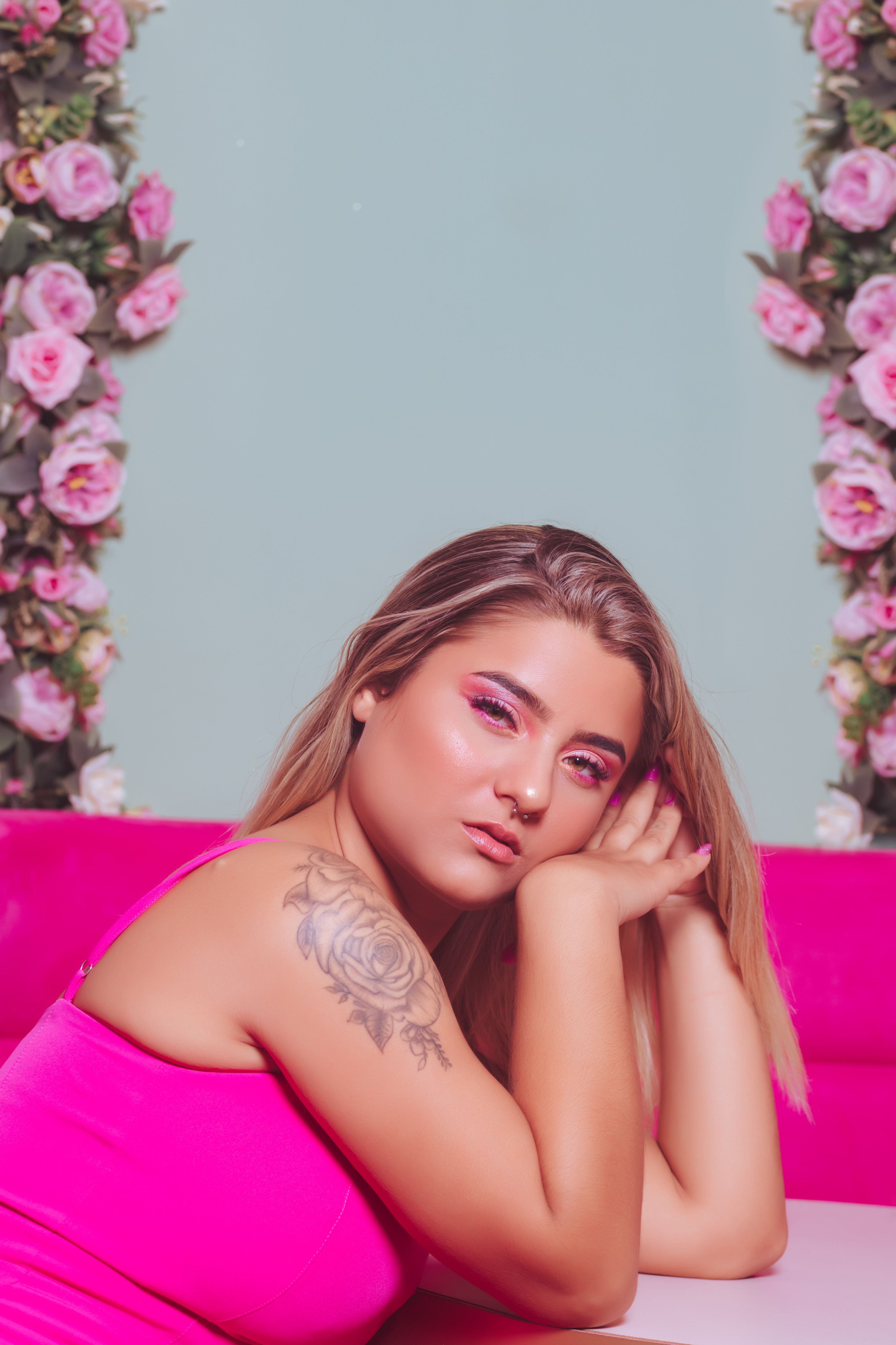 Colorful portrait of a woman with floral tattoo and pink makeup against a floral backdrop.
