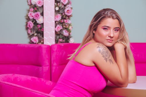 Photo of a Blonde Wearing a Pink Dress Sitting on a Pink Sofa