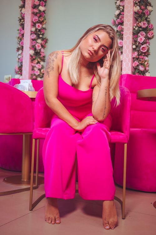 Free A fashionable woman in a pink outfit and armchair poses gracefully in a chic, floral-decorated setting. Stock Photo