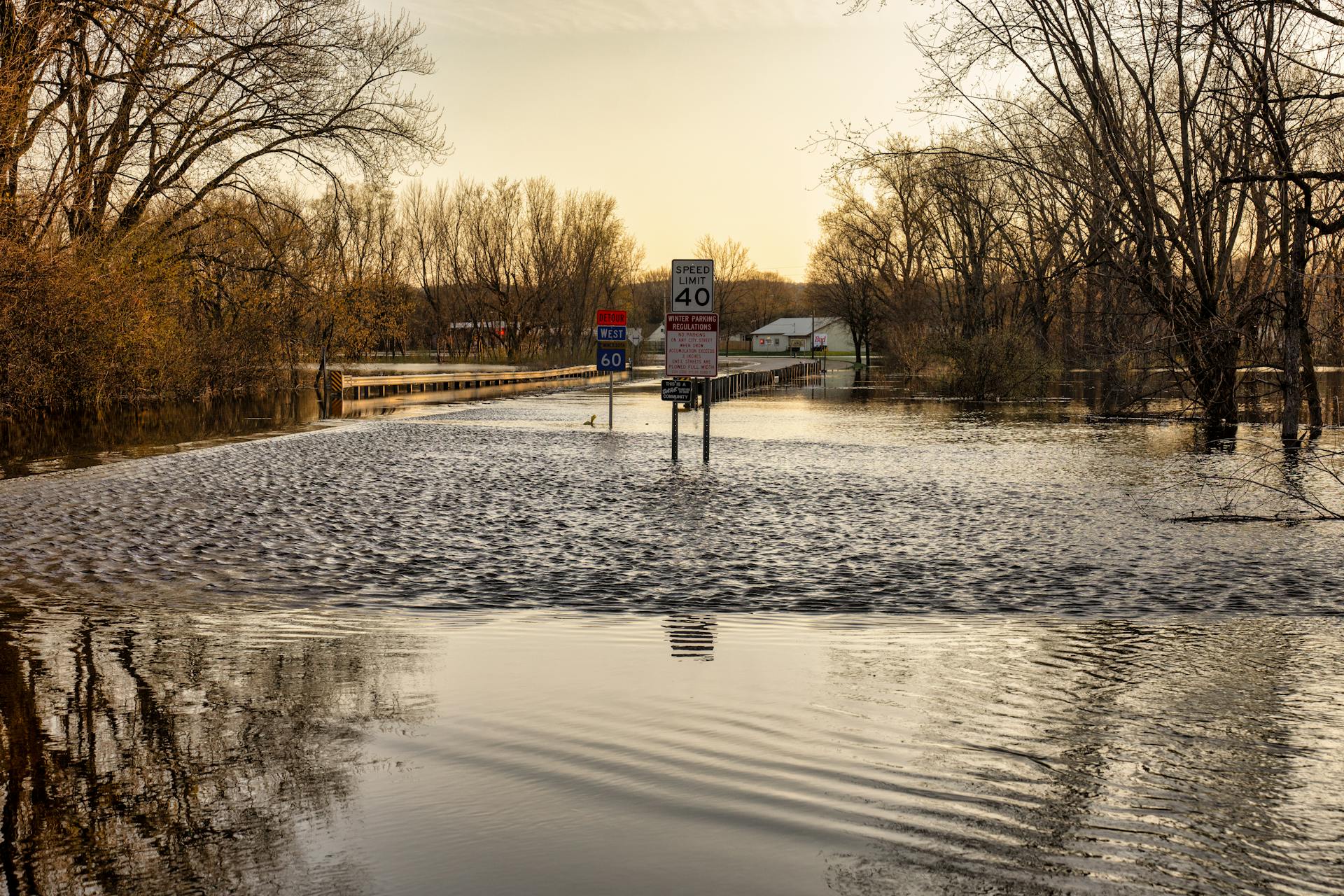 A rural road in Wabasha, MN flooded by rising river waters, with road signs partially submerged.