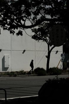 A silhouette of a man walking past a white building, surrounded by trees, creating urban contrast.