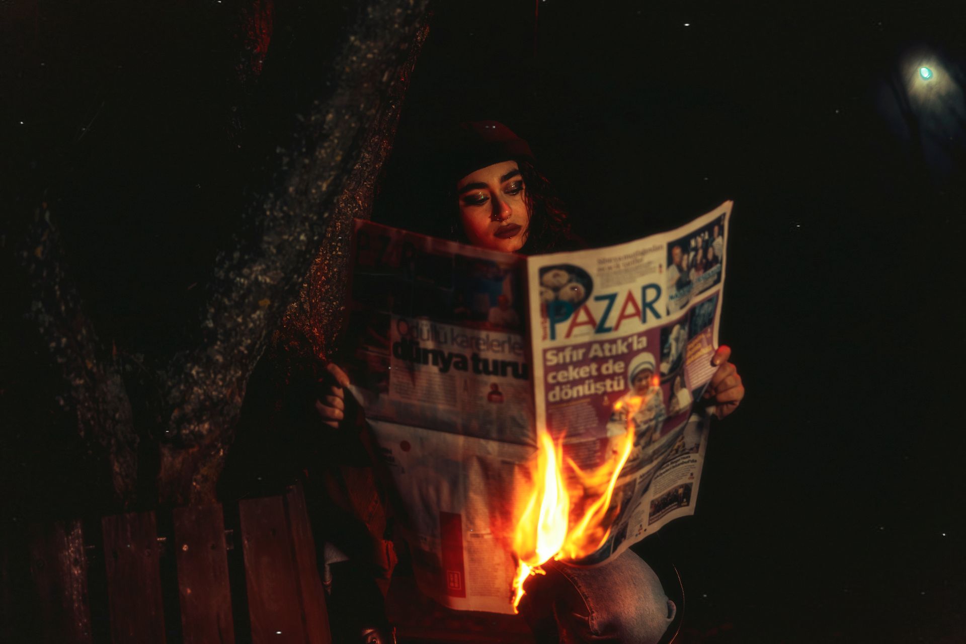 Woman Sitting in Darkness Reading Burning Newspaper