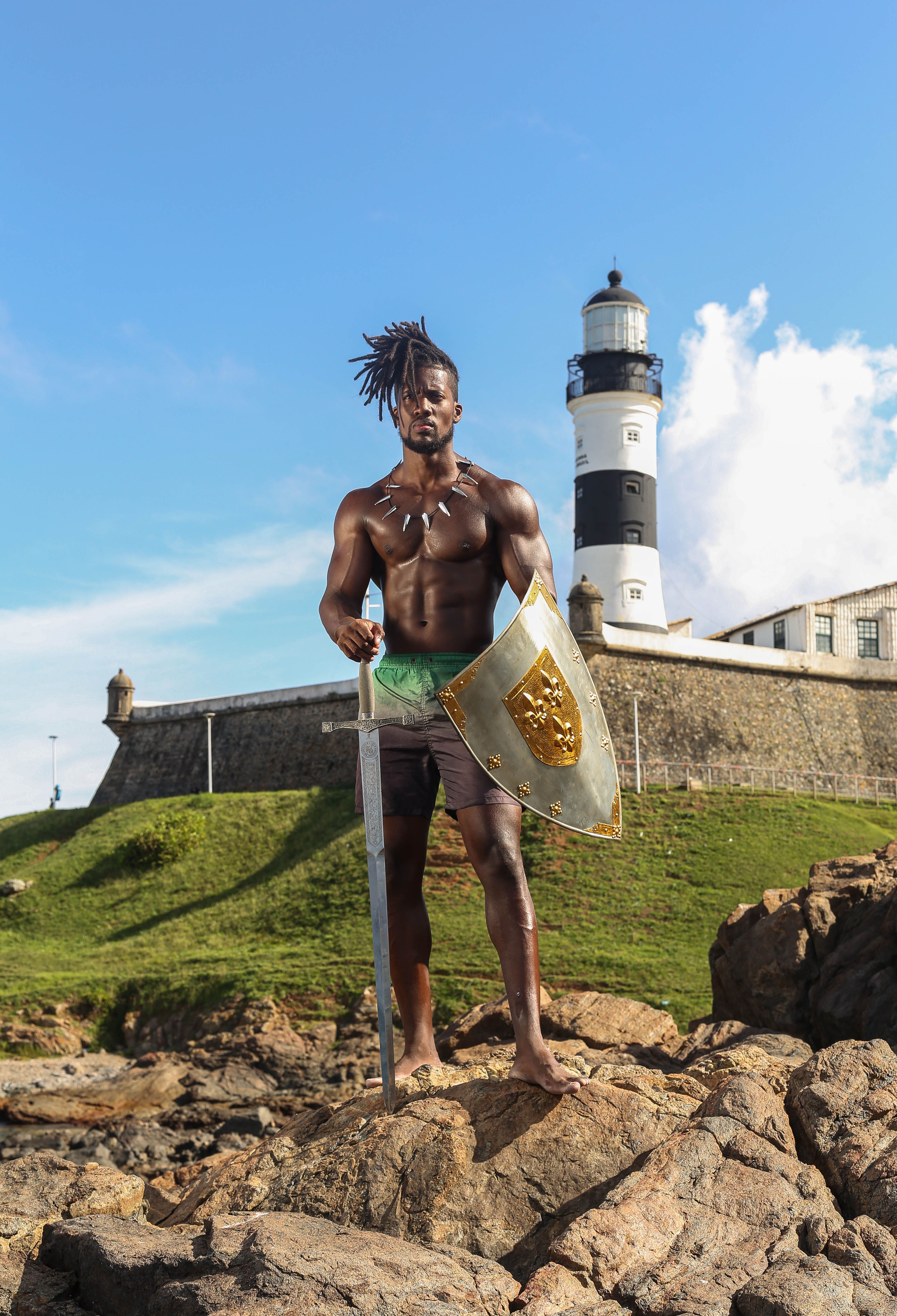 A warrior stands with a shield and sword by the historic Farol da Barra in Salvador, Brazil.