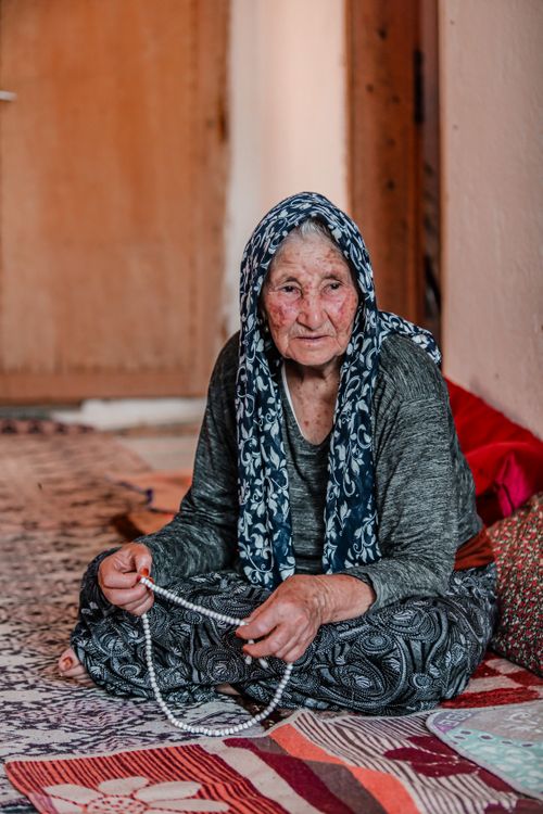 Free Senior woman with headscarf sitting indoors holding prayer beads, conveying calm and introspection. Stock Photo