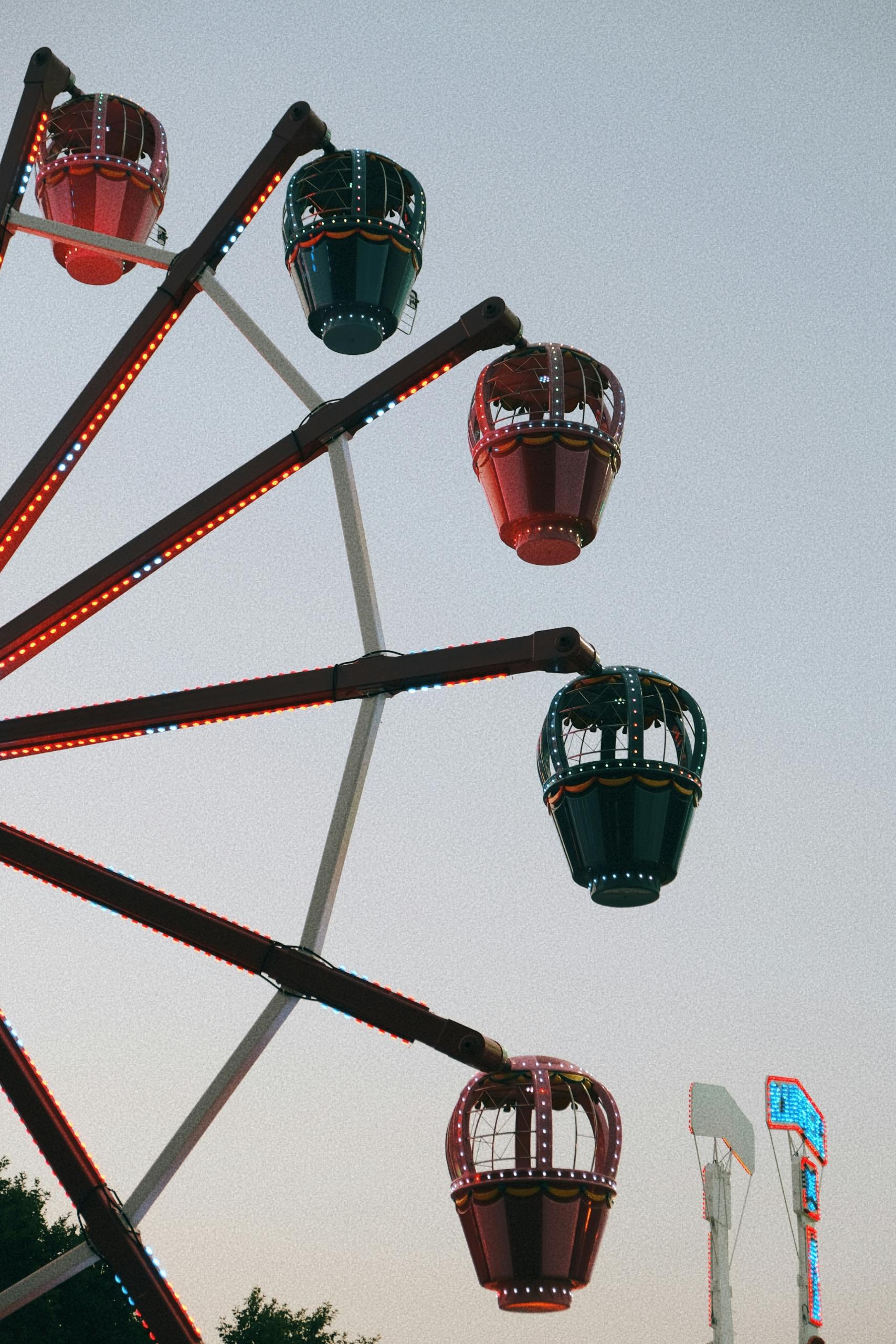 A vibrant ferris wheel with illuminated gondolas against a twilight sky at a carnival.