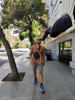 A man in casual summer wear walks along a tree-lined street in Baku, Azerbaijan.