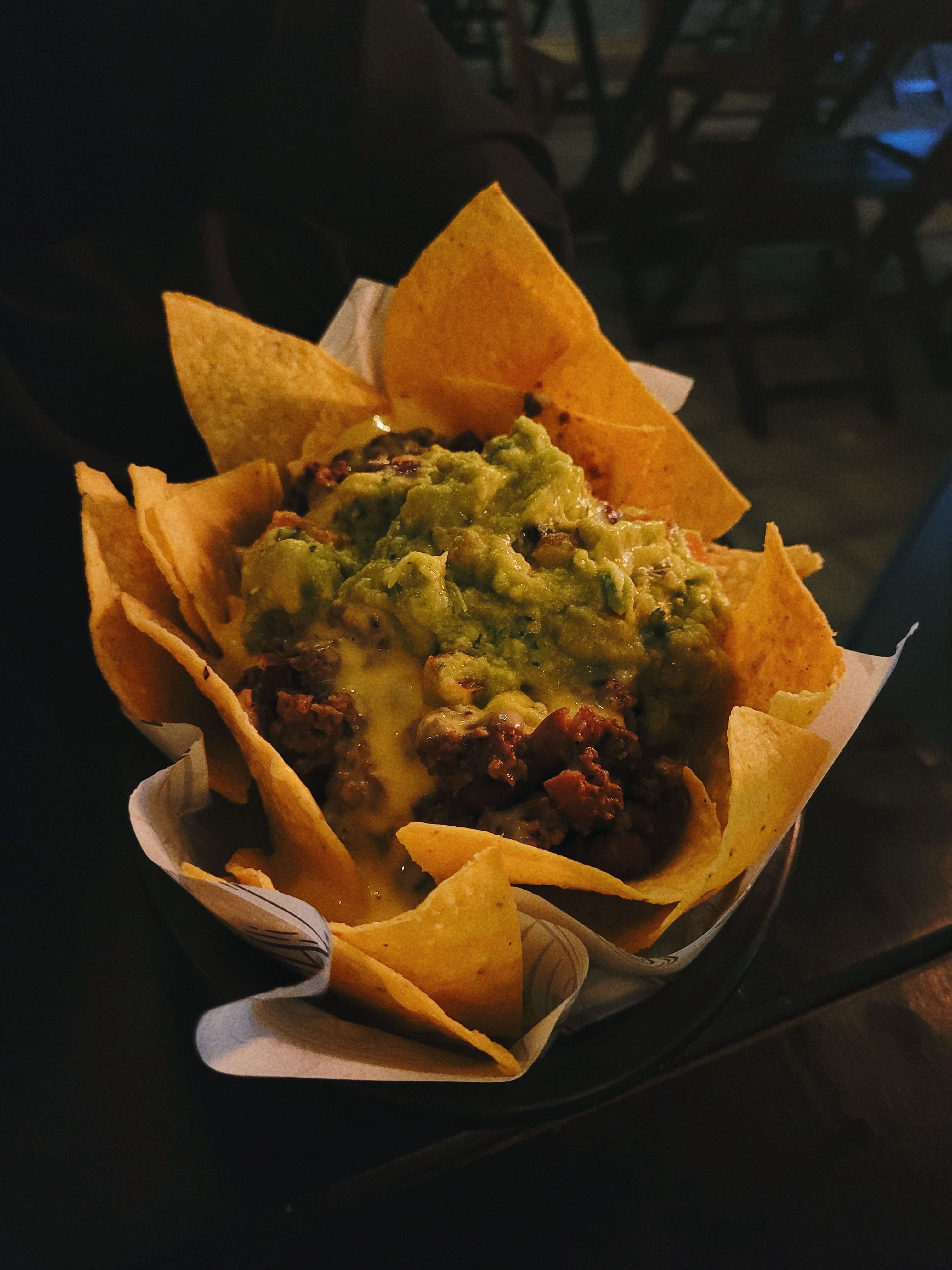 Tasty nachos topped with creamy guacamole and melted cheese in a dark, cozy setting.
