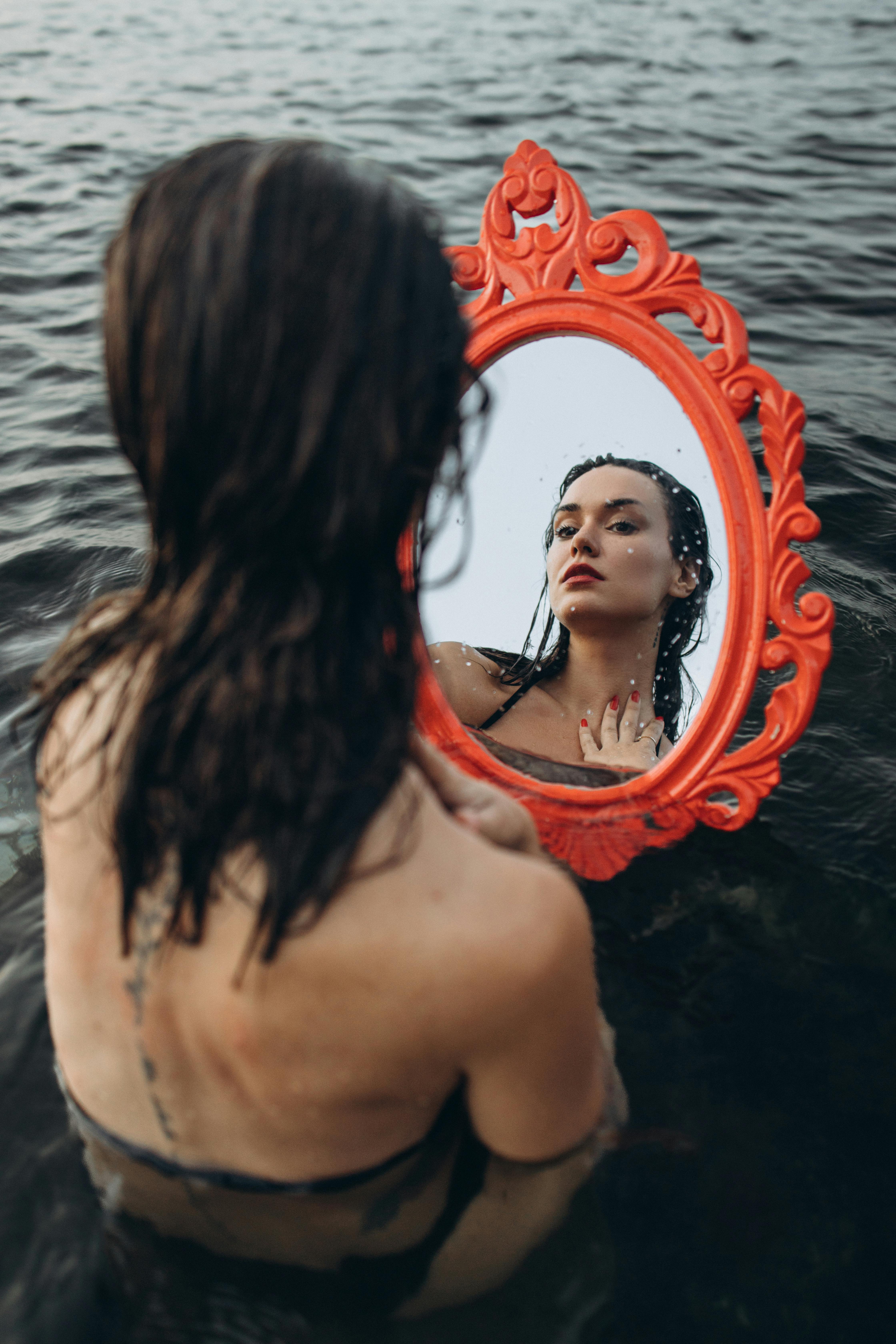 Artistic photo of a woman holding a mirror in a lake, reflecting serenity and introspection.
