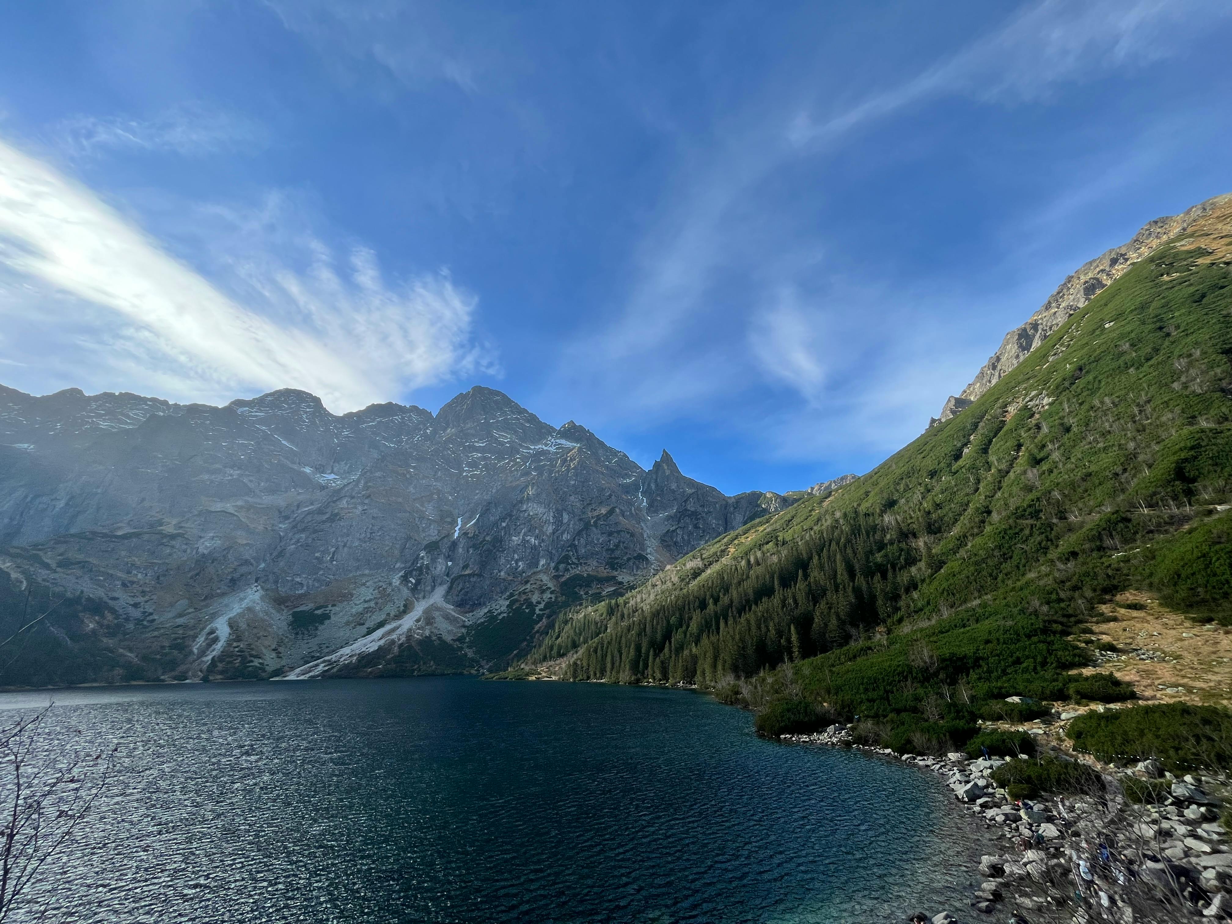 Morskie Oko Lake reflecting snow-capped Tatra Mountains at golden hour with crystal-clear waters, pine forest shoreline, and morning mist rising from the surface