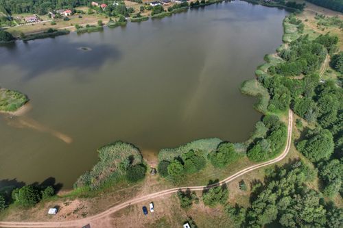 Free Drone shot of a rural lake surrounded by trees and dirt roads in a picturesque countryside setting. Stock Photo
