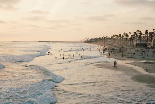 Free Serene beach scene with people enjoying the waves at sunset in California. Stock Photo