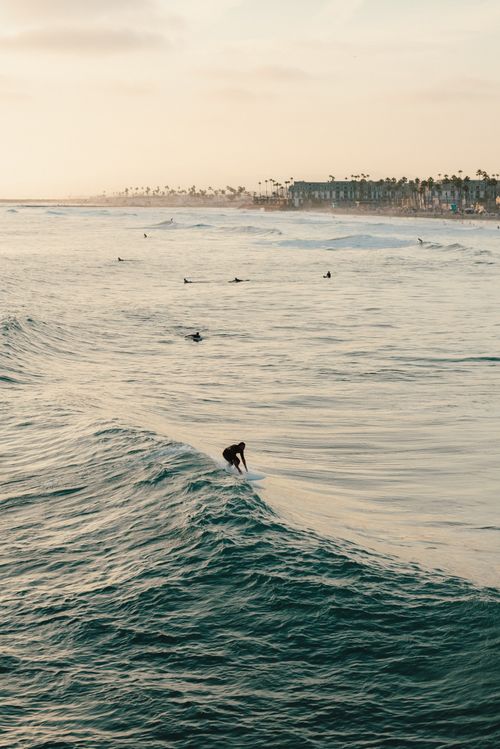 Free A surfer catches a wave at an iconic California beach during sunset, showcasing a serene coastal scene. Stock Photo