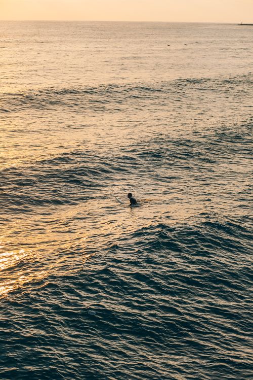 Free A lone swimmer navigates the ocean waves during a beautiful sunset, creating a serene and peaceful scene. Stock Photo