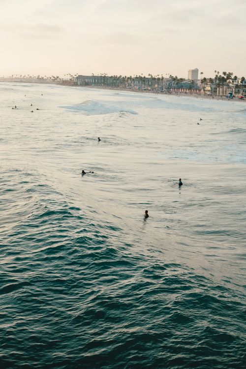 Free A serene view of surfers riding waves at sunrise near a California coastline, highlighting the beauty of coastal adventure. Stock Photo