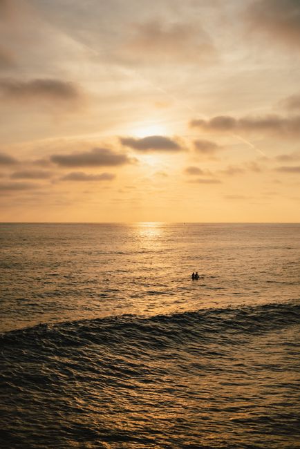 A beautiful sunset over the ocean with surfers paddling, creating a serene coastal scene.
