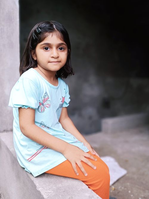 Free Charming portrait of a young girl sitting indoors, wearing a blue t-shirt and orange pants. Stock Photo