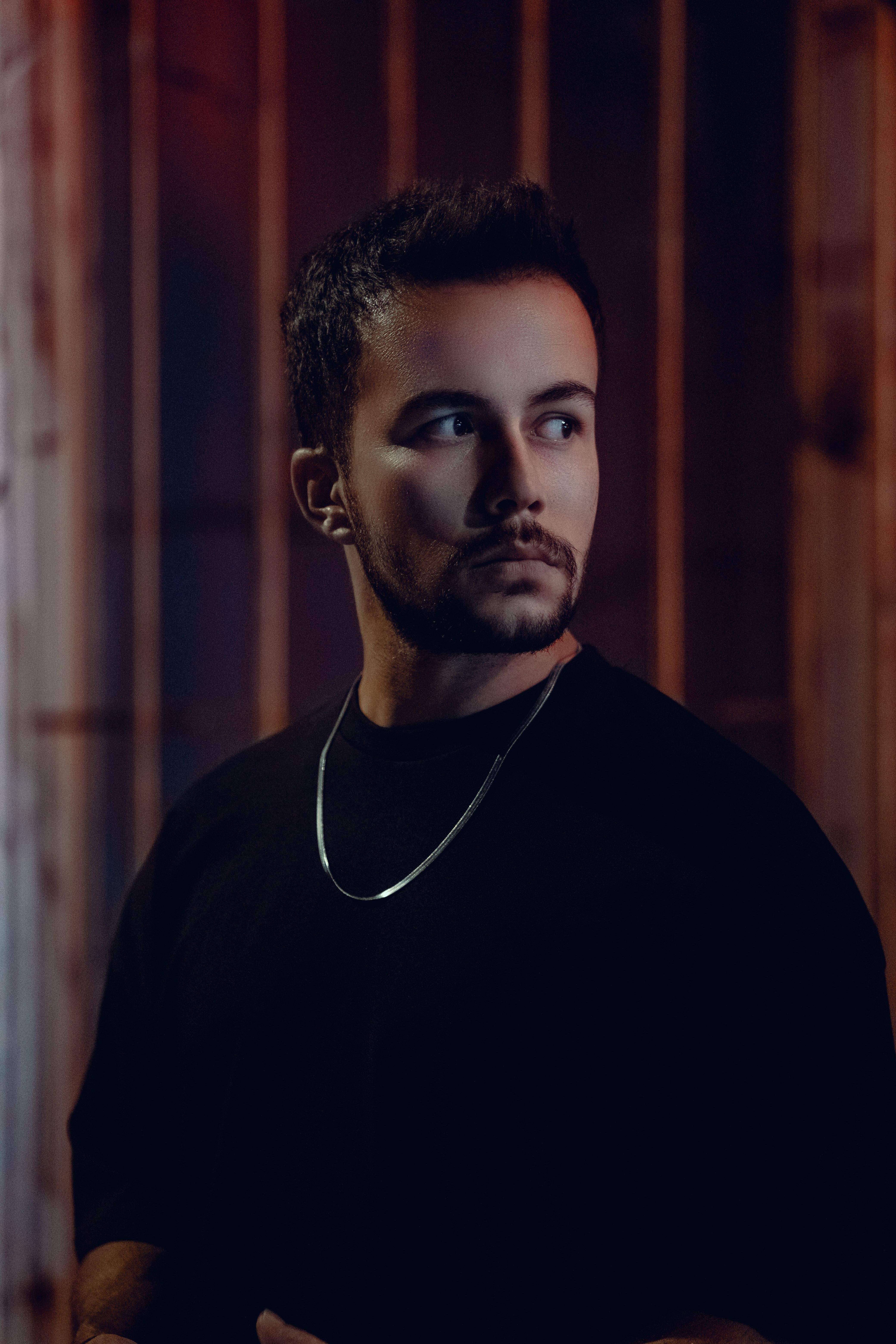 Stylish portrait of a man with short hair and a necklace, exuding a moody atmosphere.