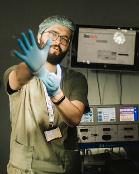 A male surgeon in scrubs and gloves, extending hand in a hospital setting.