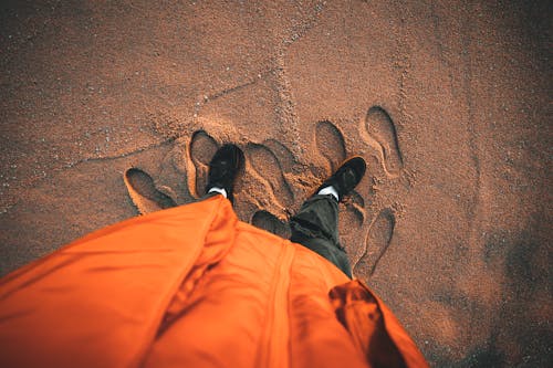 Person in Orange Jacket Stands on Sand