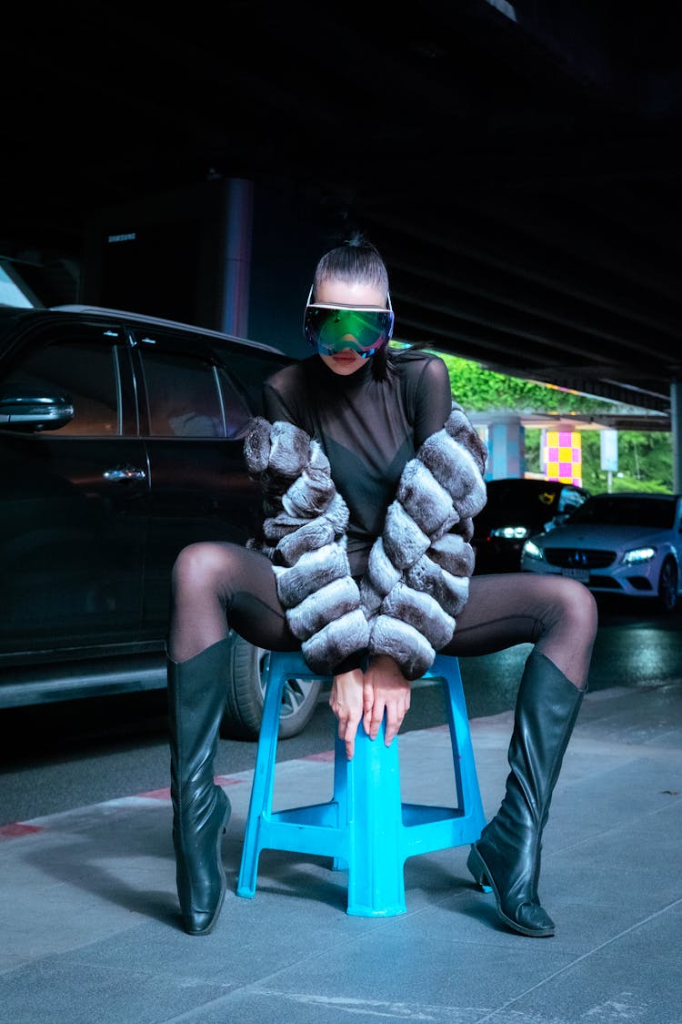 Woman In Goggles Sitting On Chair On Sidewalk At Night